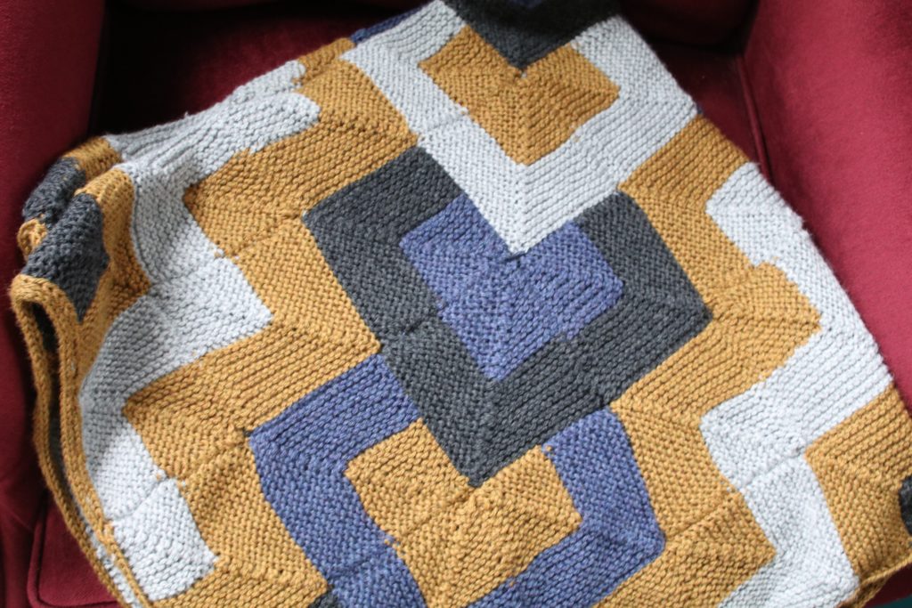 Image of the Tamarix Quilt by Heather Zoppetti, knit in gray, gold, charcoal, and blue