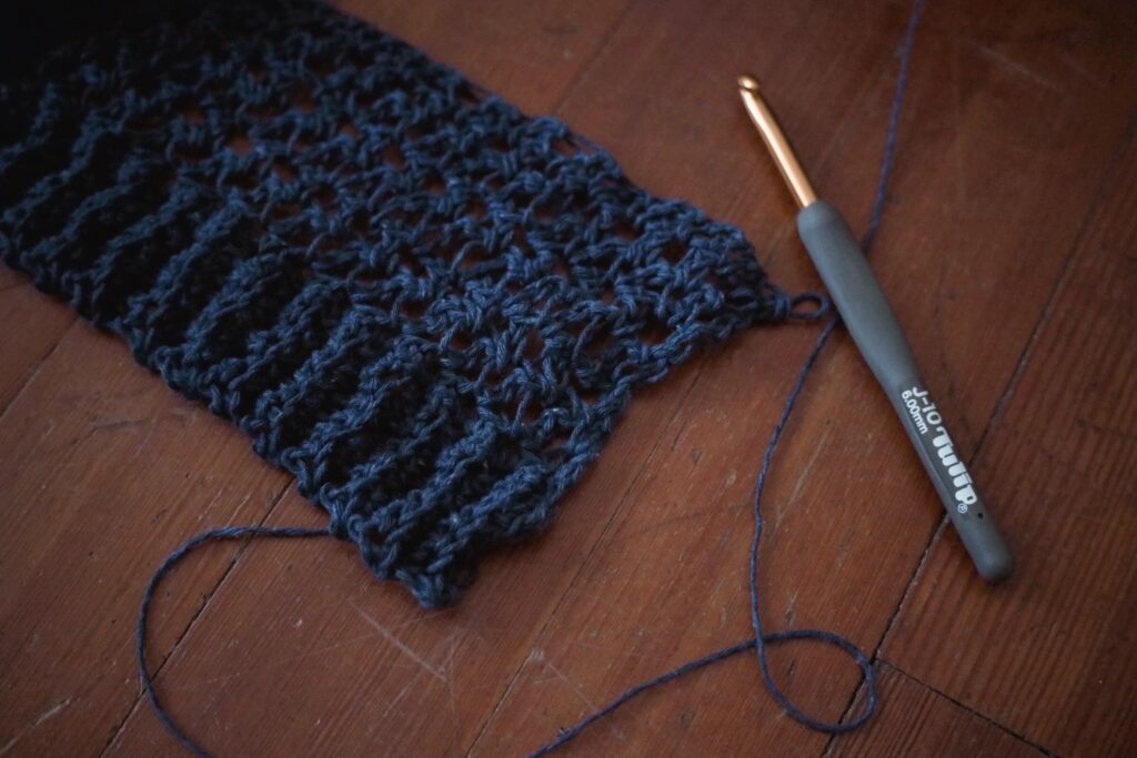 Beginning of a crochet project using a blue yarn and a J hook.