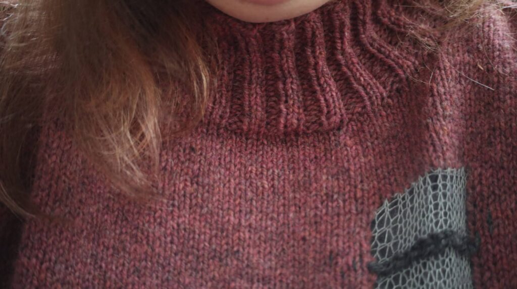 Close up shot of a knitted sweater, showing the ribbed neckline and a section of an intarsia detail.