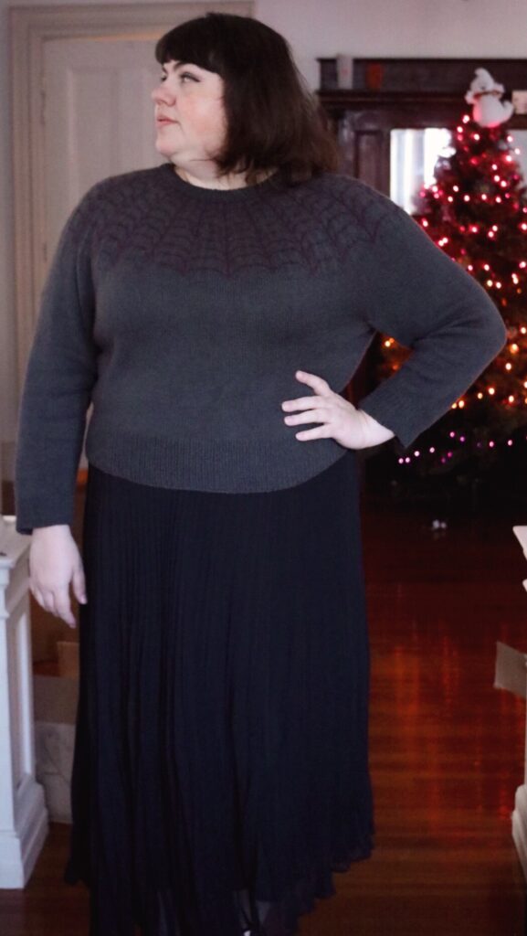 Photo of Amy modeling her Arachne Sweater. One hand is on a hip and she is looking to the side.