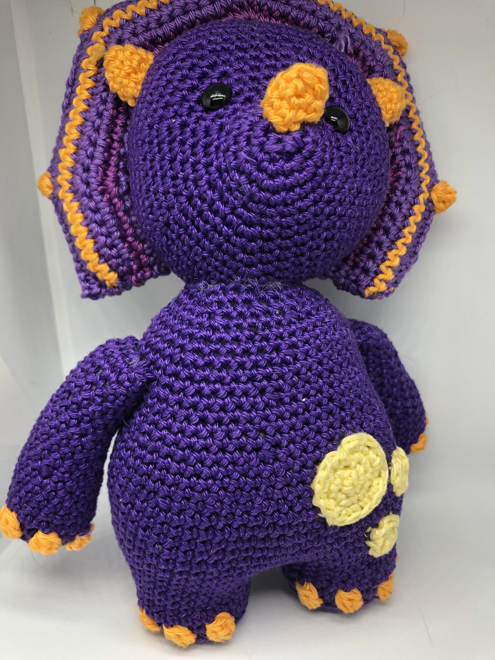 Picture of Tessa the Triceratops a crochet dinosaur amigurumi. Tessa is purple with orange claws and yellow spots. 