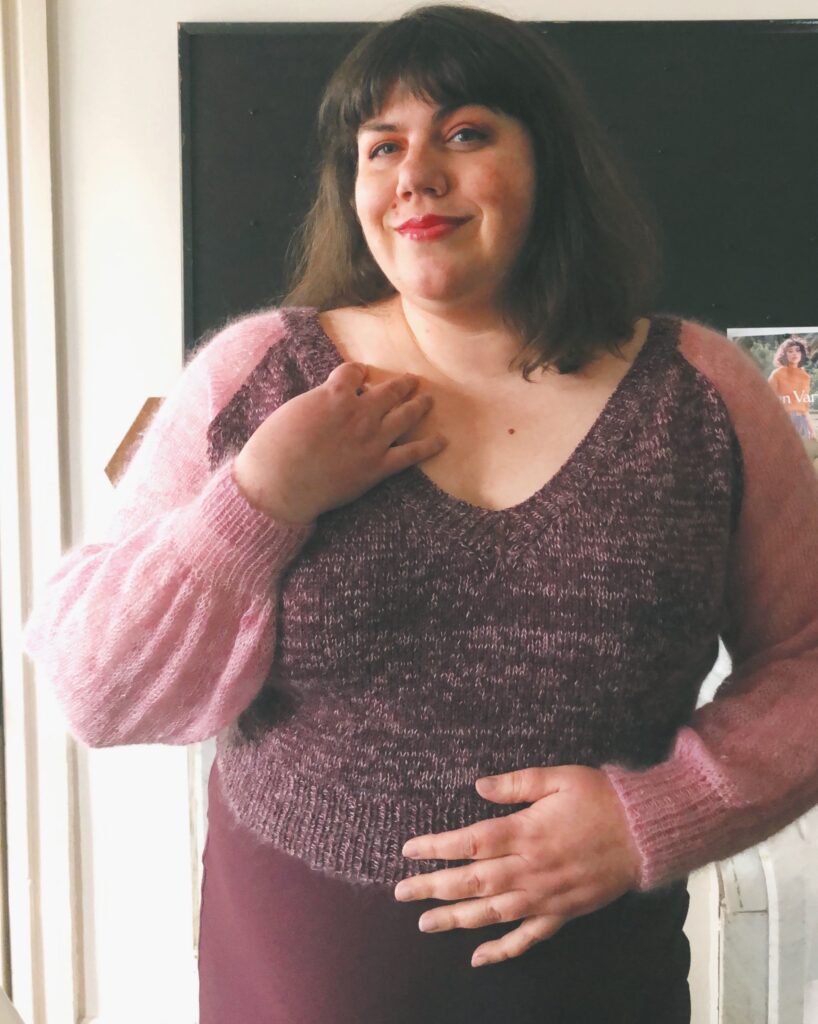 Amy,a small-fat white woman, models her Diaphanous Raglan. The sleeves are a rosy pink and the body is a combination of the same rosy pink and a deep red-purple shade.