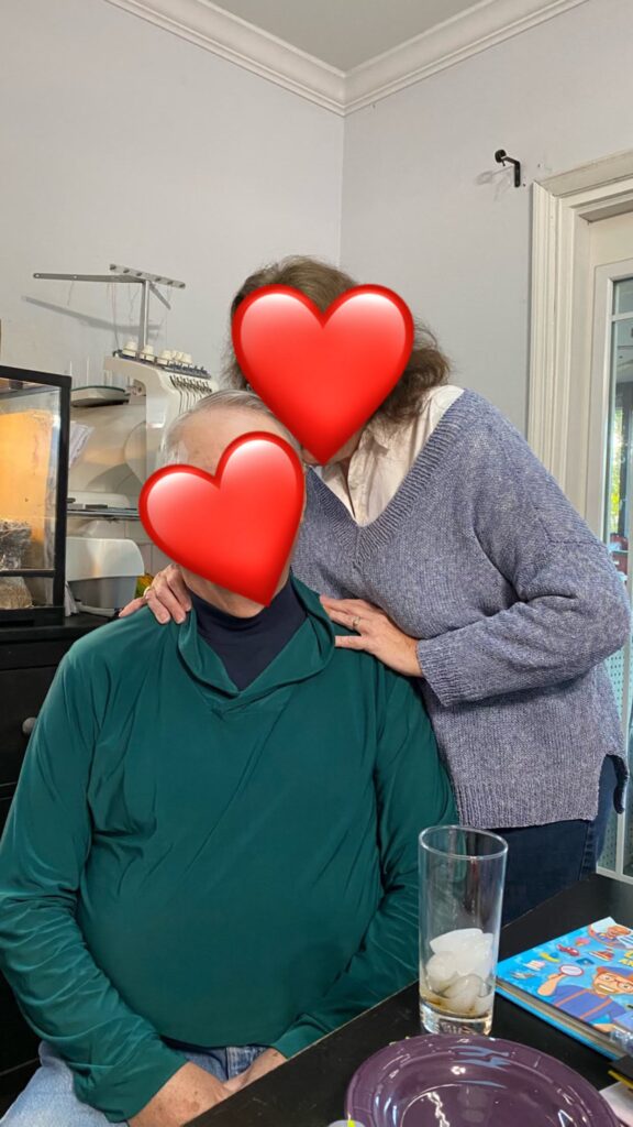 Photo of Amy's parents with hearts over their faces. Her mom is modeling her light blue Sevilla sweater over a white button down top, and her father is wearing an Amy-made green sweater over a blue turtleneck. 