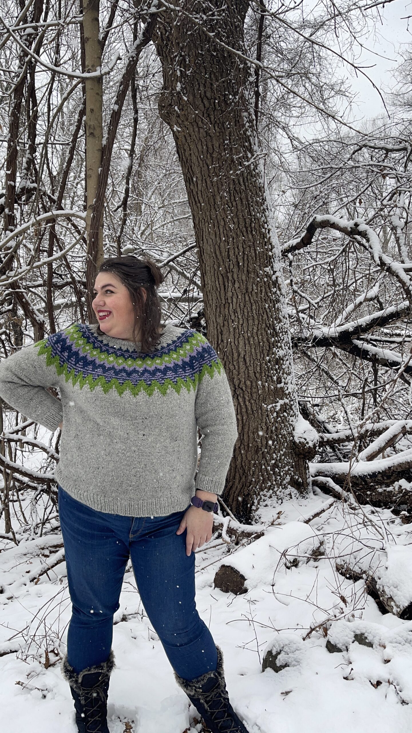 Amy standing in the middle of the woods, during a light snow storm, wearing her Kordy Sweater